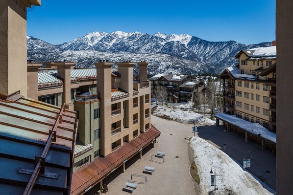 A hotel with multiple floors, a covered outdoor area with benches, and a view of snow-covered mountains in the background. - Updated Ski in/Ski Out Condo - Corner Unit - Two Decks - Awesome Slope Views (Durango)