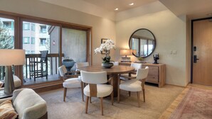 A dining area with a round table, white chairs, a bowl of flowers, and a large mirror on the wall.