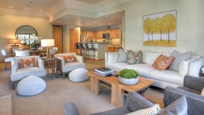 A modern living room with a sofa, armchairs, a coffee table, and a dining area with a kitchen in the background.