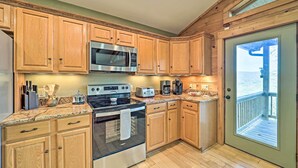 Una cocina con armarios de madera, electrodomésticos de acero inoxidable y vistas al exterior a través de una puerta.