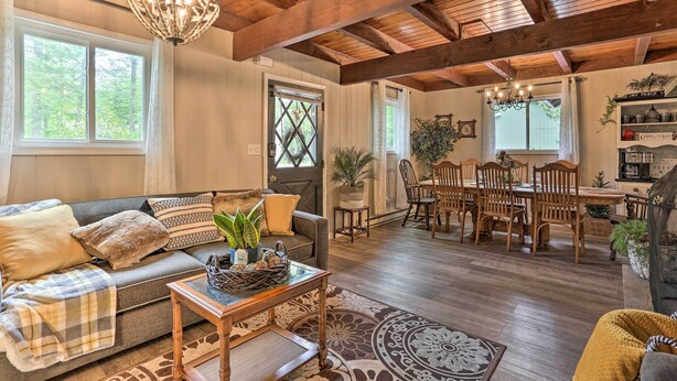 A cozy living room with a wooden ceiling, a dining area with wooden chairs, and a large window with a view of trees. - Welcoming Poconos Retreat w/ Deck & Pool Access (Tobyhanna)