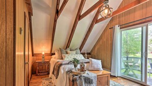 A cozy bedroom with a wooden ceiling, a bed with pillows and a bedside table, a nightstand, and a view of the outdoors through a sliding glass door. - Welcoming Poconos Retreat w/ Deck & Pool Access (Tobyhanna)
