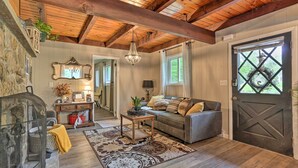 A cozy living room with a wooden ceiling, a grey sofa, a patterned rug, and a large window with a view of greenery. - Welcoming Poconos Retreat w/ Deck & Pool Access (Tobyhanna)