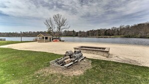 A lakeside property with a sandy beach, a wooden deck, and a small shed. - Welcoming Poconos Retreat w/ Deck & Pool Access (Tobyhanna)