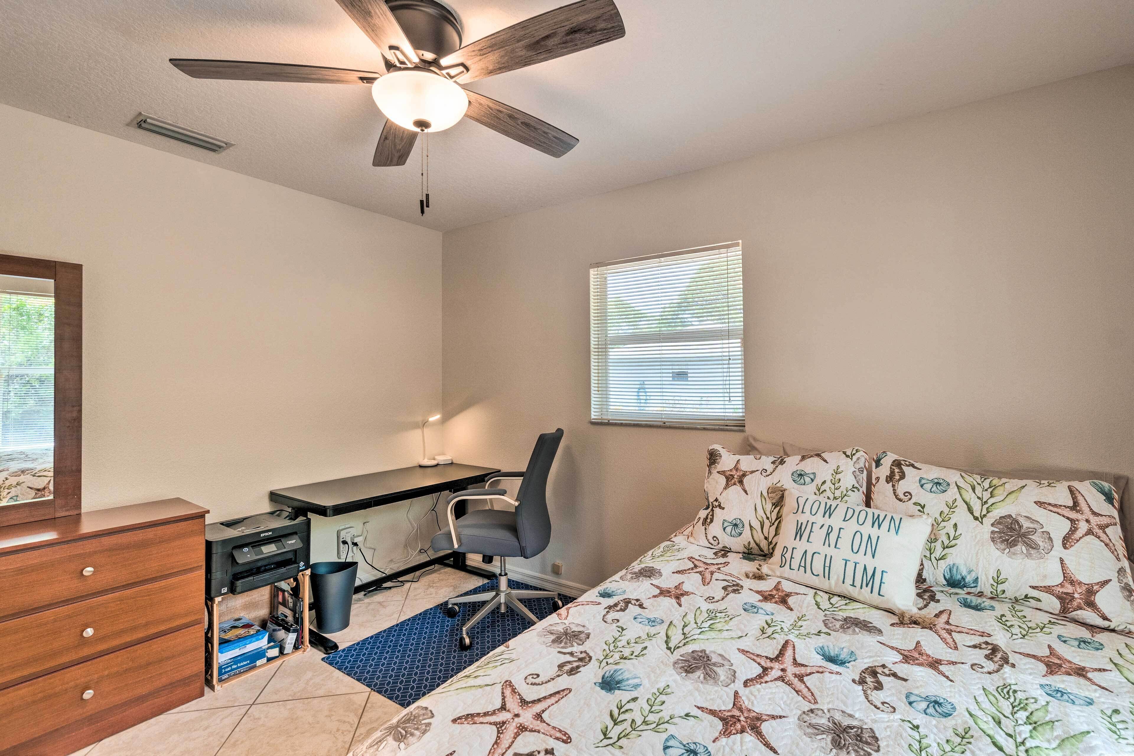 A bedroom with a bed, desk, chair, dresser, and a ceiling fan.