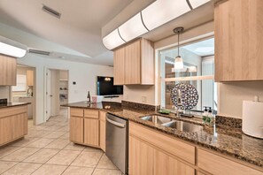 A modern kitchen with granite countertops, wooden cabinets, a dishwasher, and a large window with a decorative mirror.