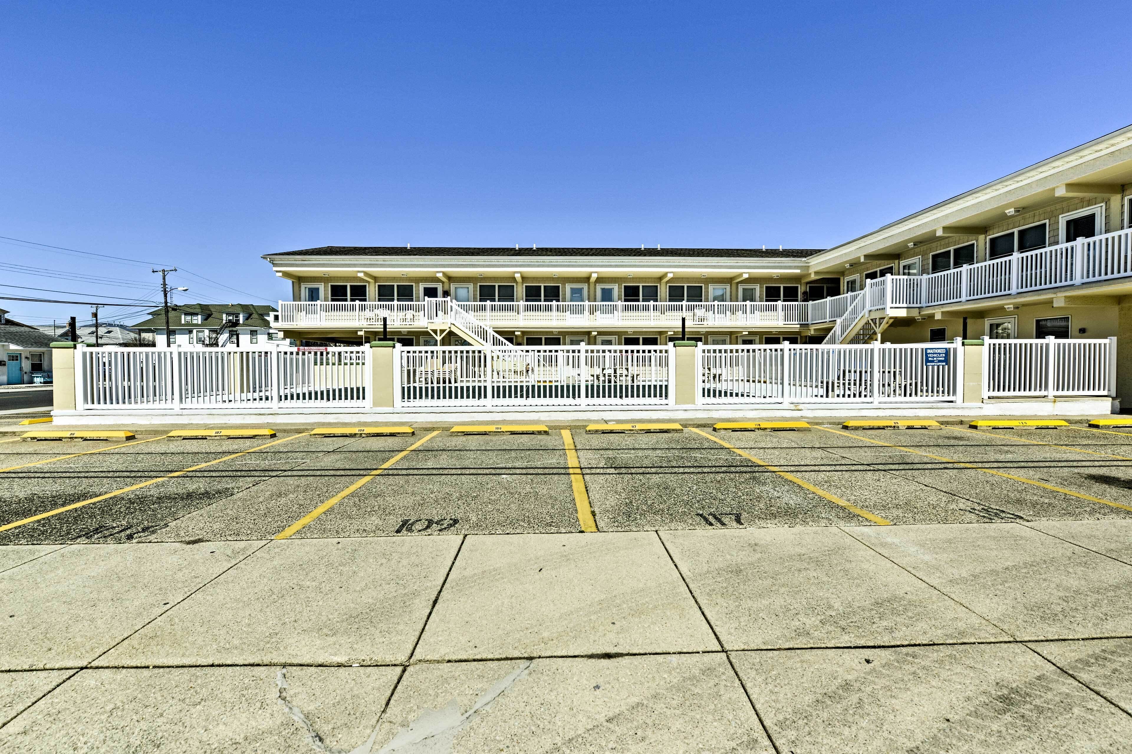 A multi-story hotel with a balcony on the second floor, a parking lot with marked spaces, and a clear blue sky.