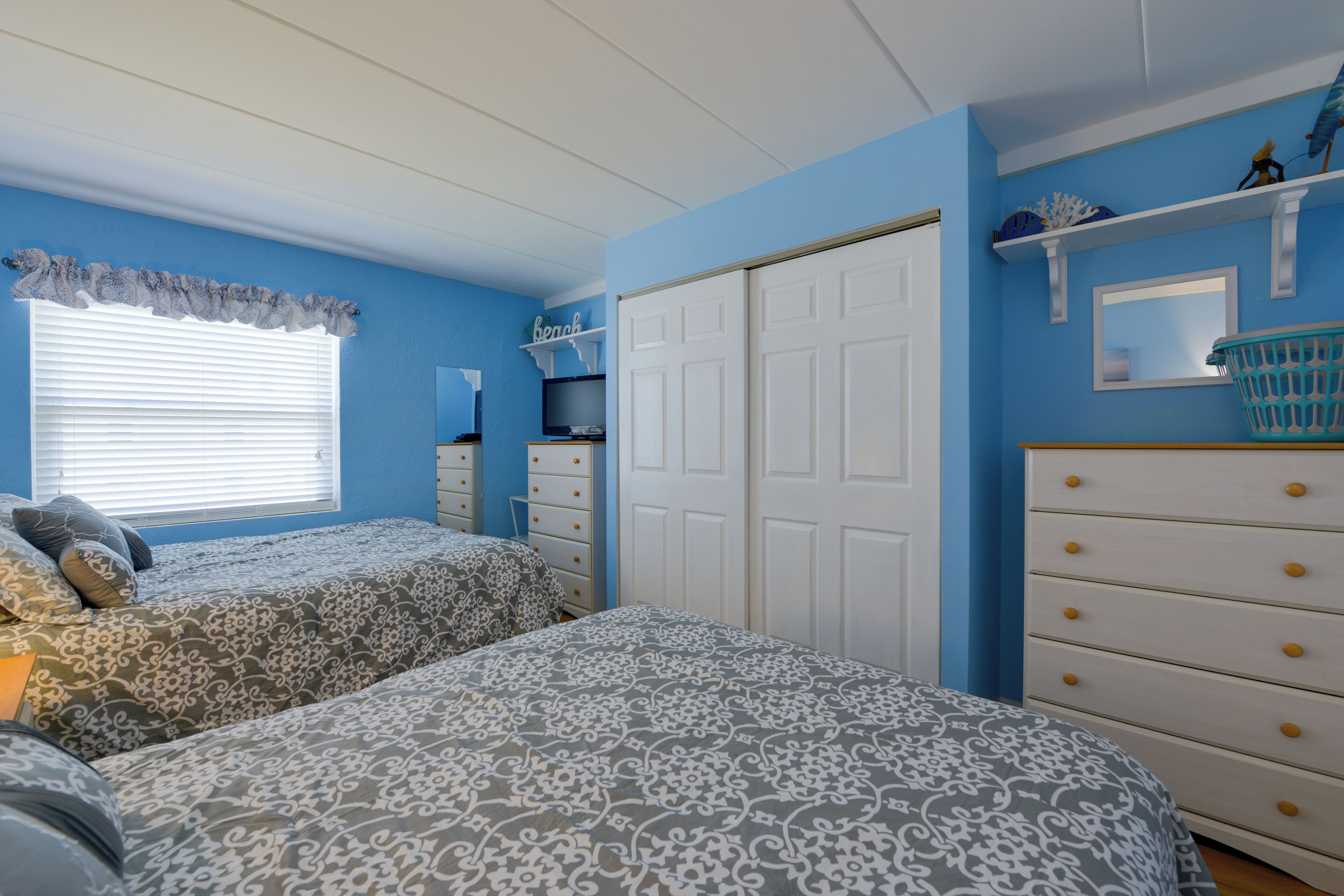 A bedroom with two beds, a wardrobe, and a shelf with decorative items.