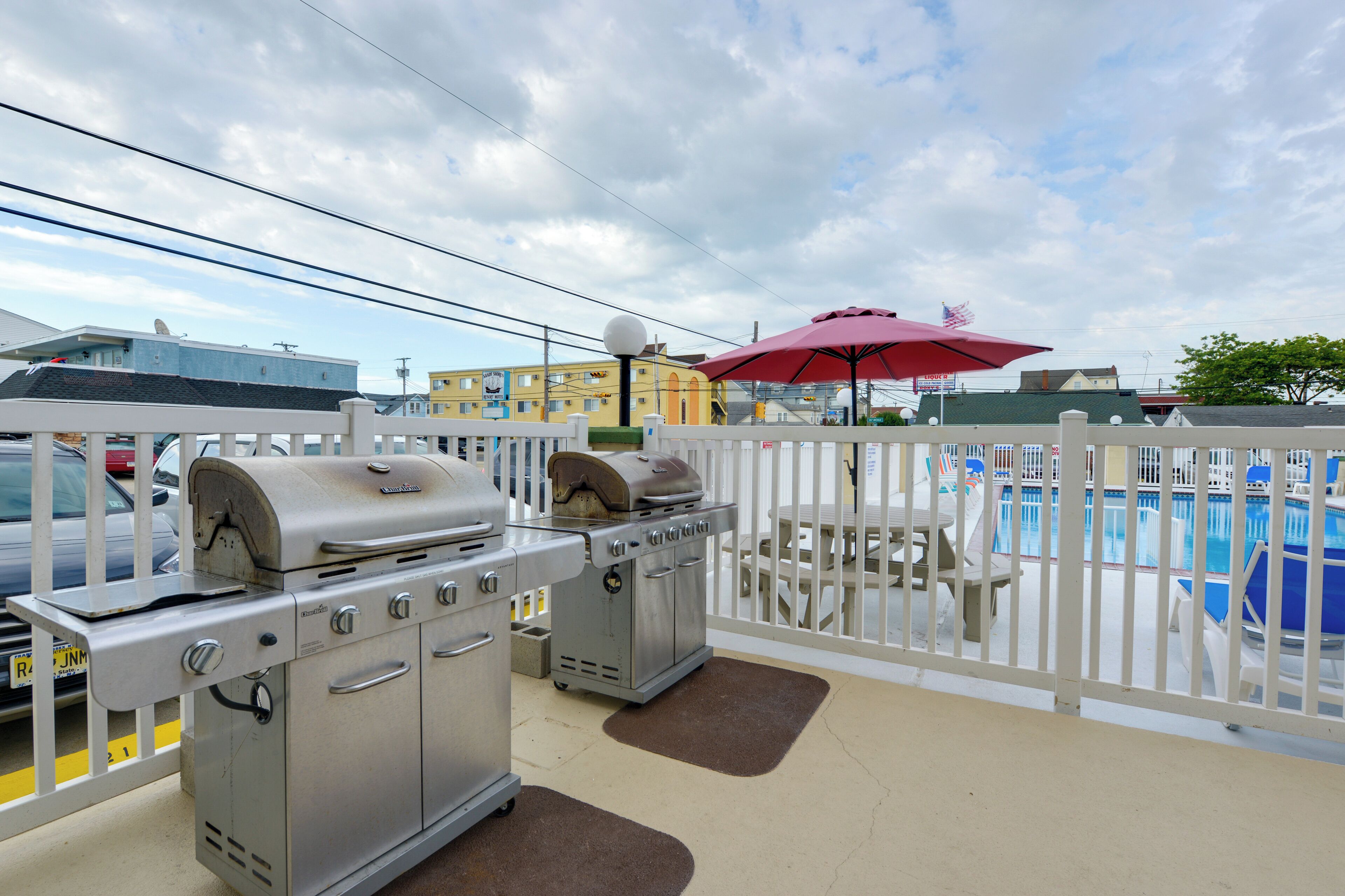 A balcony with a barbecue grill, a pool, and a red umbrella.