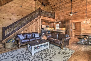 A log cabin interior with a staircase, leather sofas, a coffee table, and a kitchen area. - 8 Mi to Dtwn Murphy! Cabin w/ Nottely River Views (Murphy)