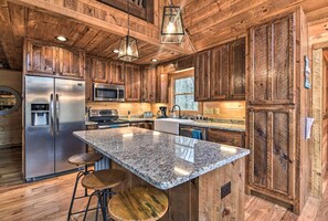 A kitchen with wooden cabinets, a stainless steel refrigerator, a granite countertop, and bar stools. - 8 Mi to Dtwn Murphy! Cabin w/ Nottely River Views (Murphy)