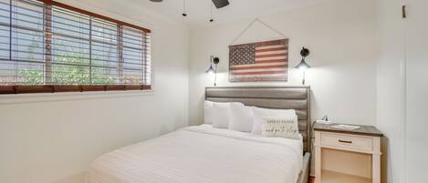 A bedroom with a bed, a nightstand, a ceiling fan, a window with blinds, and an American flag decoration.