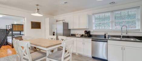 Una cocina moderna con armarios blancos, una mesa de comedor de madera y un lavavajillas integrado.