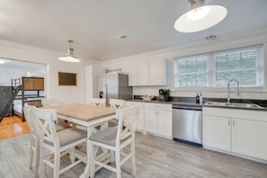 A modern kitchen with white cabinetry, a wooden dining table, and a built-in dishwasher. - Family-friendly Knoxville Home: Close to UT! (Knoxville)
