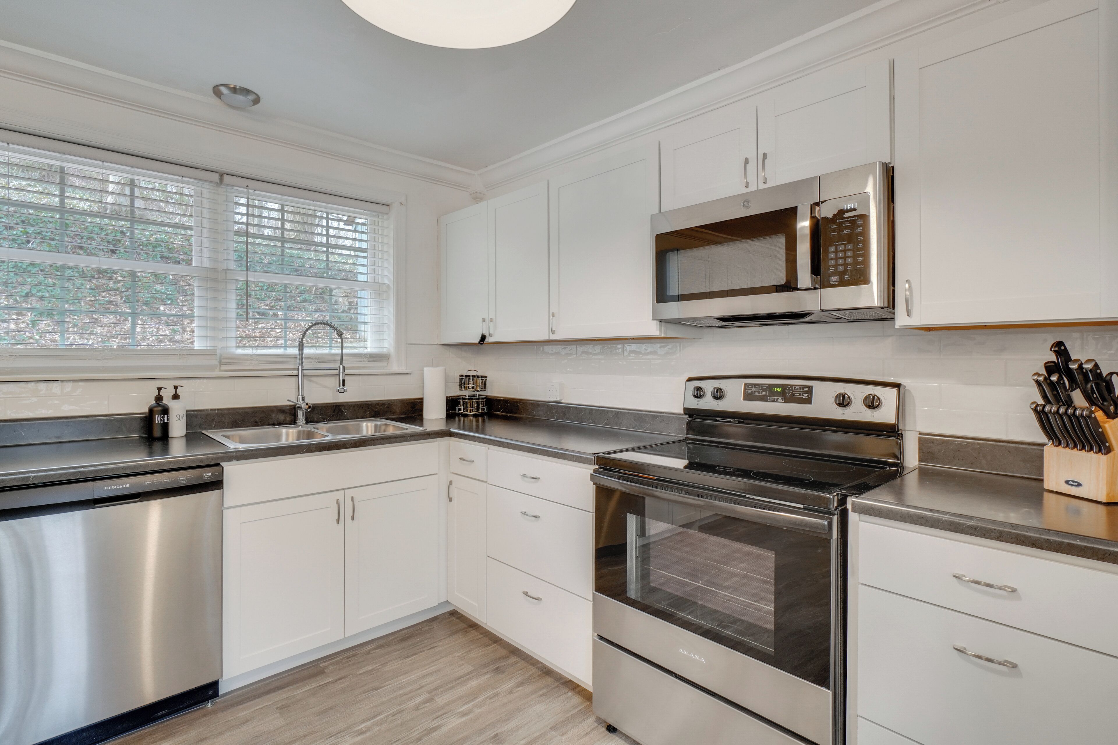 A modern kitchen with stainless steel appliances, white cabinetry, and a window with blinds.