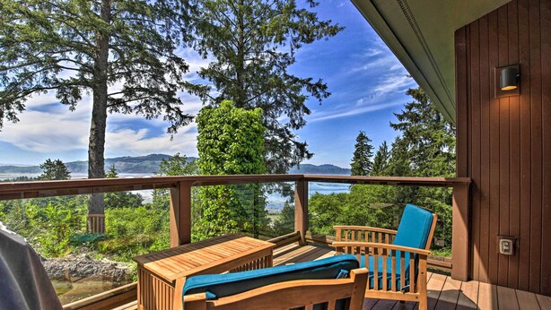 A wooden deck with a view of a forest and mountains. There are two wooden chairs with cushions. - Luxe Coastal Haven w/ Bay Views & Hot Tub (Bay City)