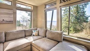 A modern living room with a sectional sofa, large windows, and a painting on the wall. - Luxe Coastal Haven w/ Bay Views & Hot Tub (Bay City)