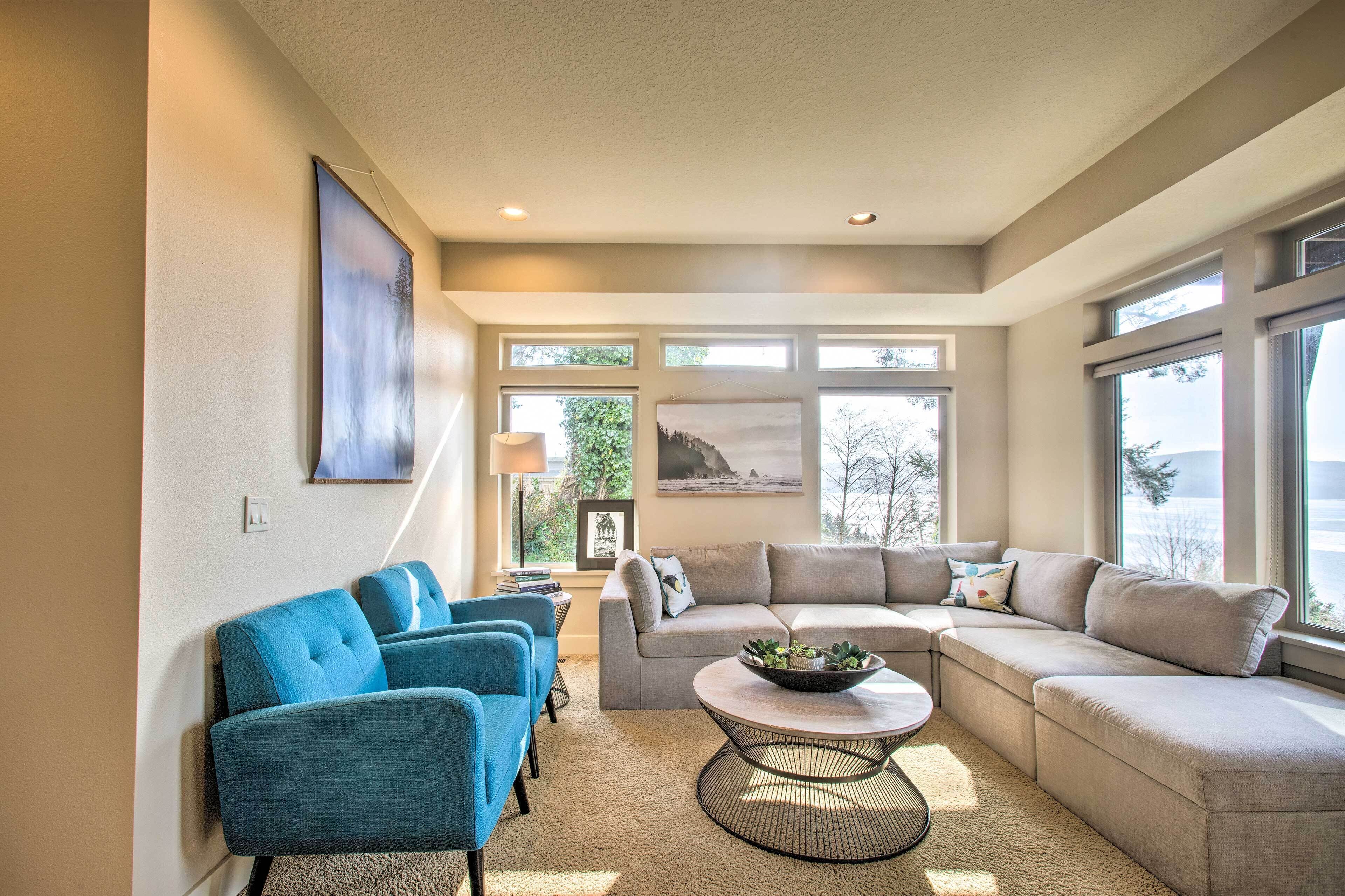 A modern living room with a sectional sofa, two blue armchairs, and a round coffee table.