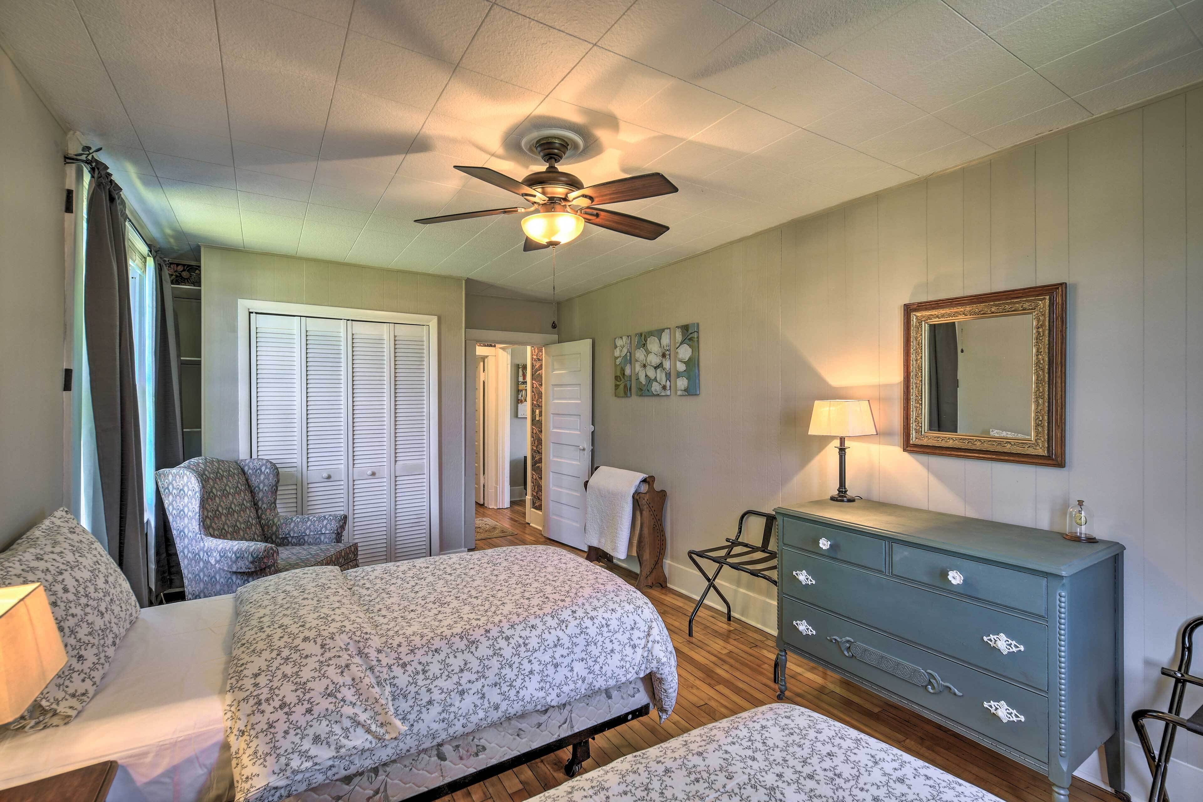 A bedroom with two beds, a ceiling fan, a dresser, a chair, and a mirror.