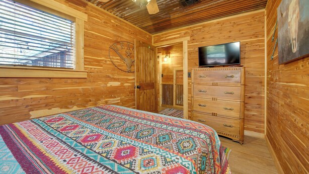 A wooden cabin room with a bed, a dresser, a television, and a ceiling fan. - Private Hot Tub & Deck! Broken Bow Group Getaway (Broken Bow)