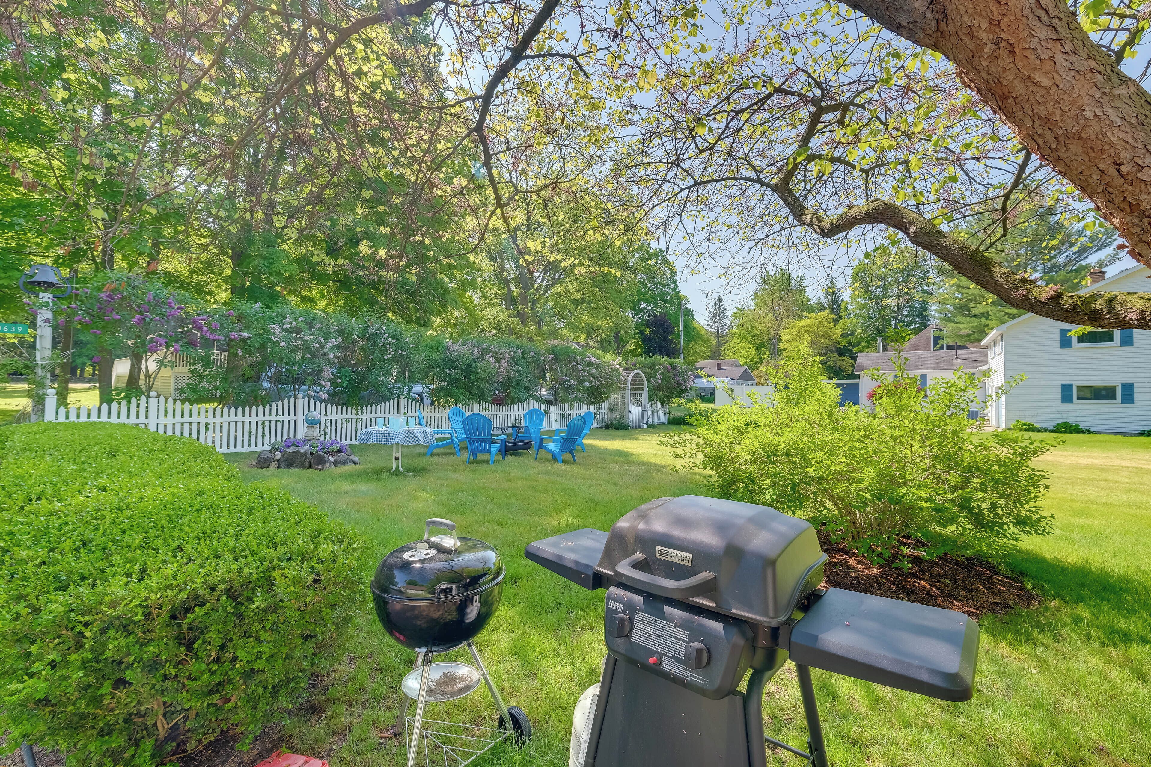 A backyard with a grill, a white fence, and a small tree.