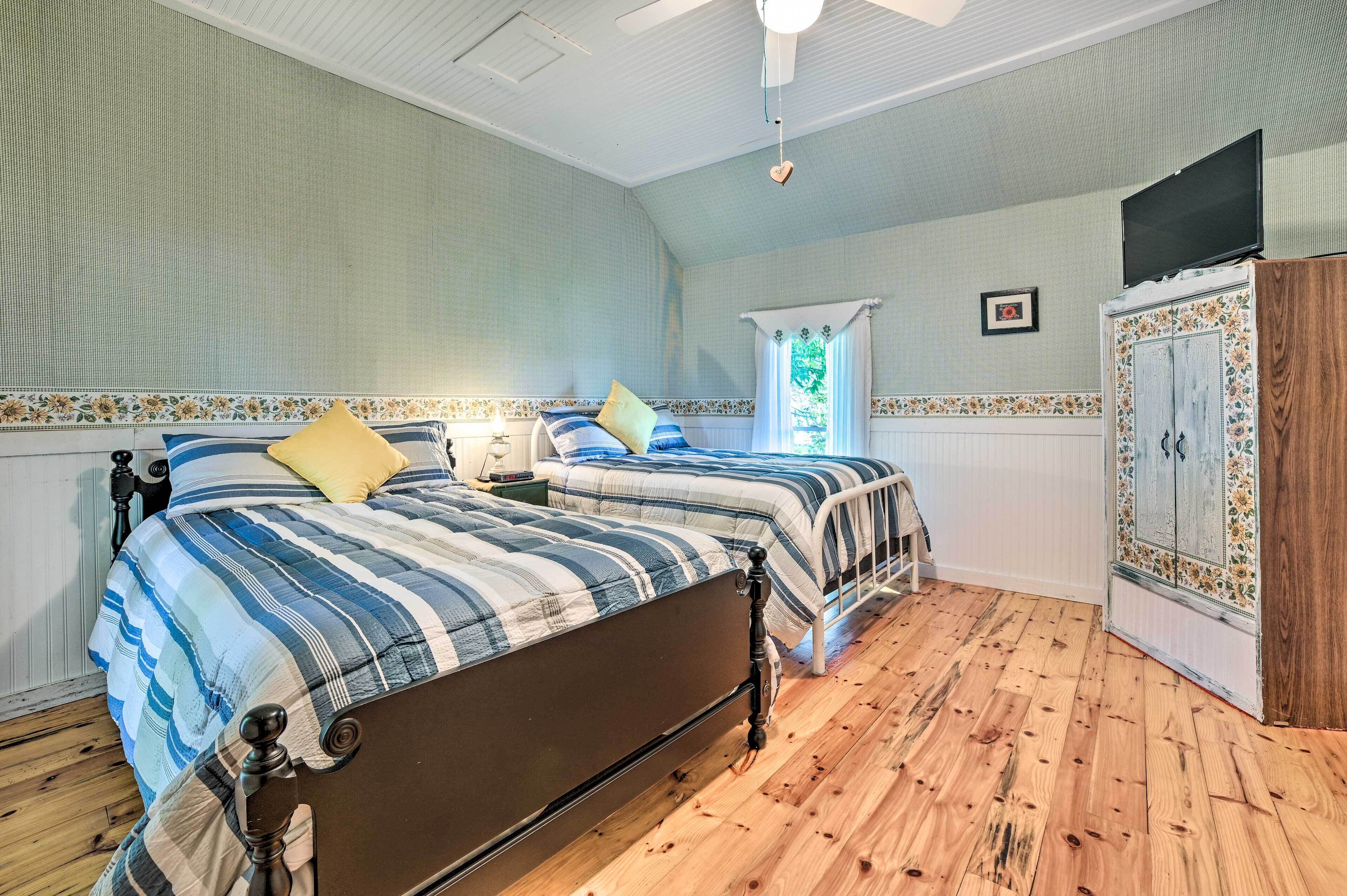 Une chambre avec deux lits, un plancher en bois, un ventilateur de plafond, une armoire et une fenêtre avec des rideaux.