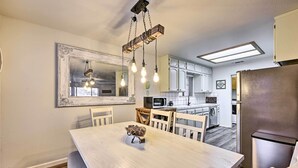 Une cuisine moderne avec des meubles blancs, un réfrigérateur en acier inoxydable et un coin repas comprenant une table et des chaises en bois.