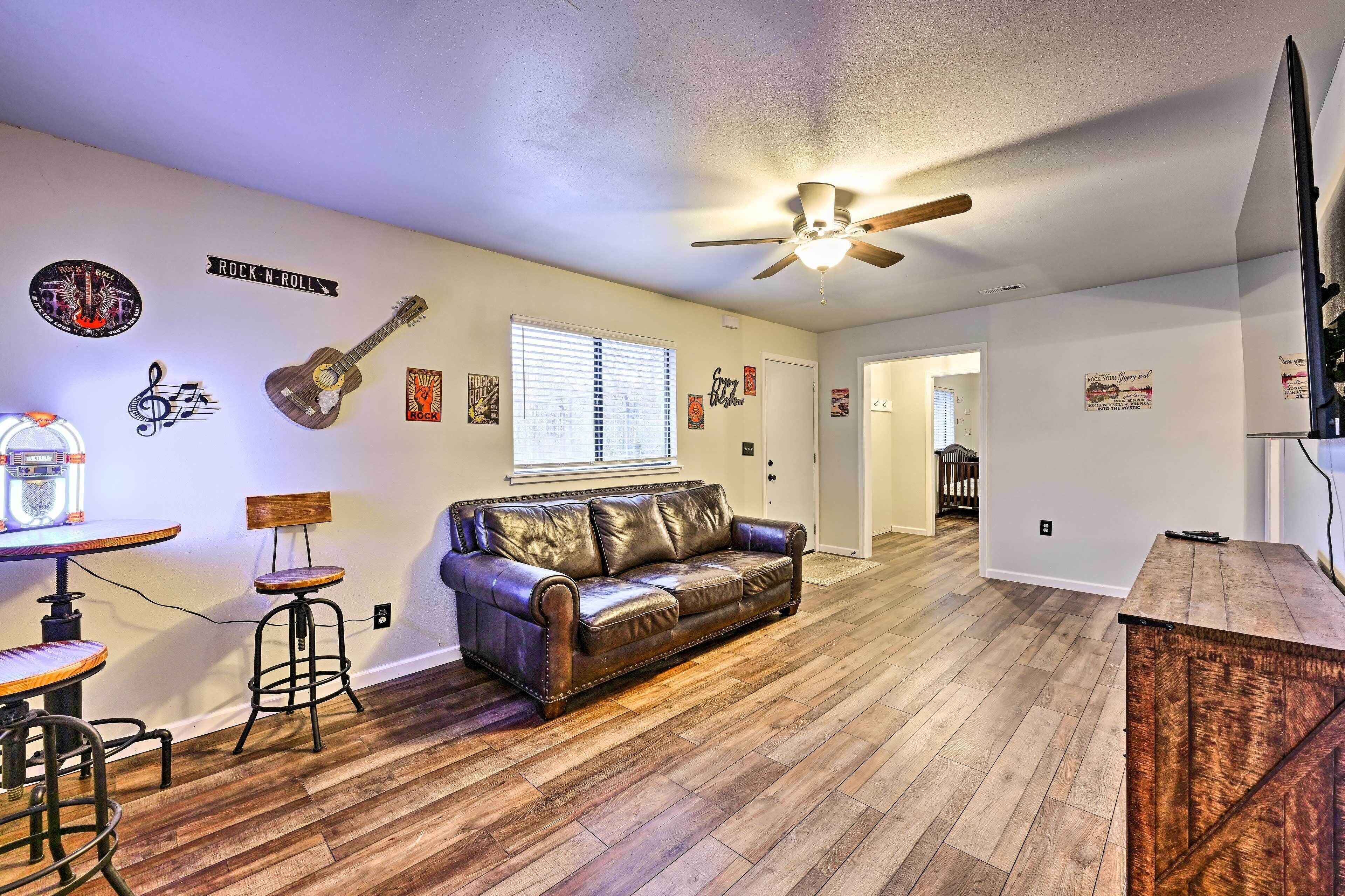 A living room with a leather couch, wooden flooring, and a ceiling fan.