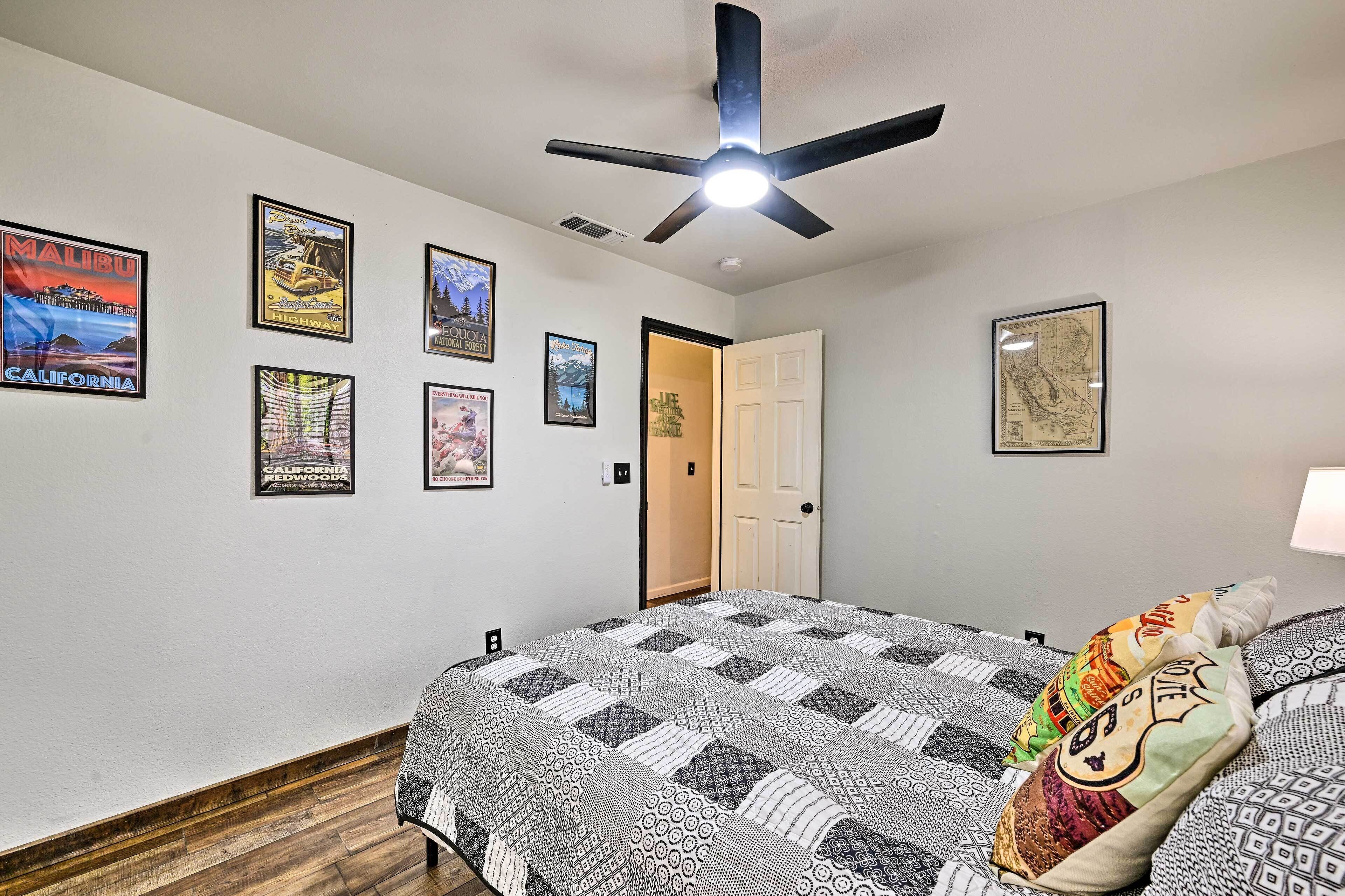 A bedroom with a bed, a ceiling fan, and various framed posters on the wall.