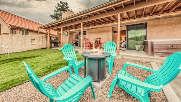Ein Patio im Freien mit einem Feuerkorb, vier türkisfarbenen Stühlen und einem überdachten Sitzbereich.