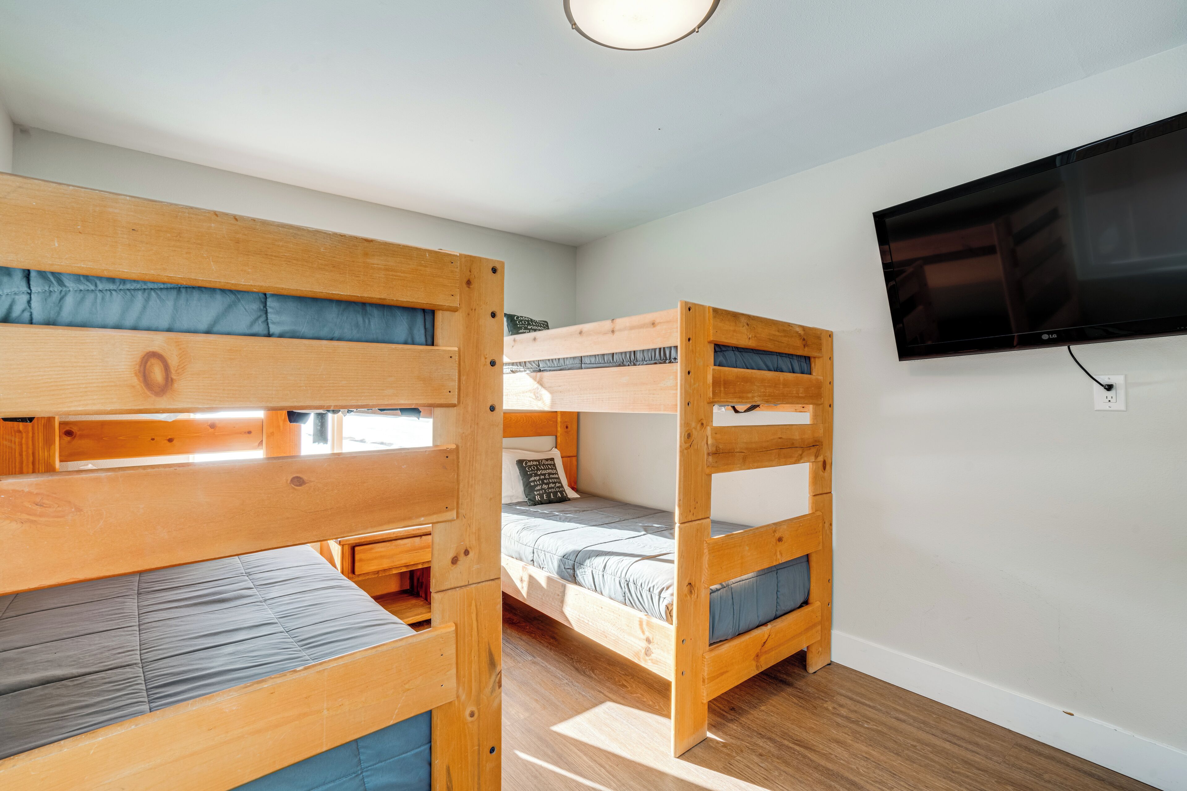 Une chambre avec des lits superposés, un téléviseur à écran plat fixé au mur et un plancher en bois.
