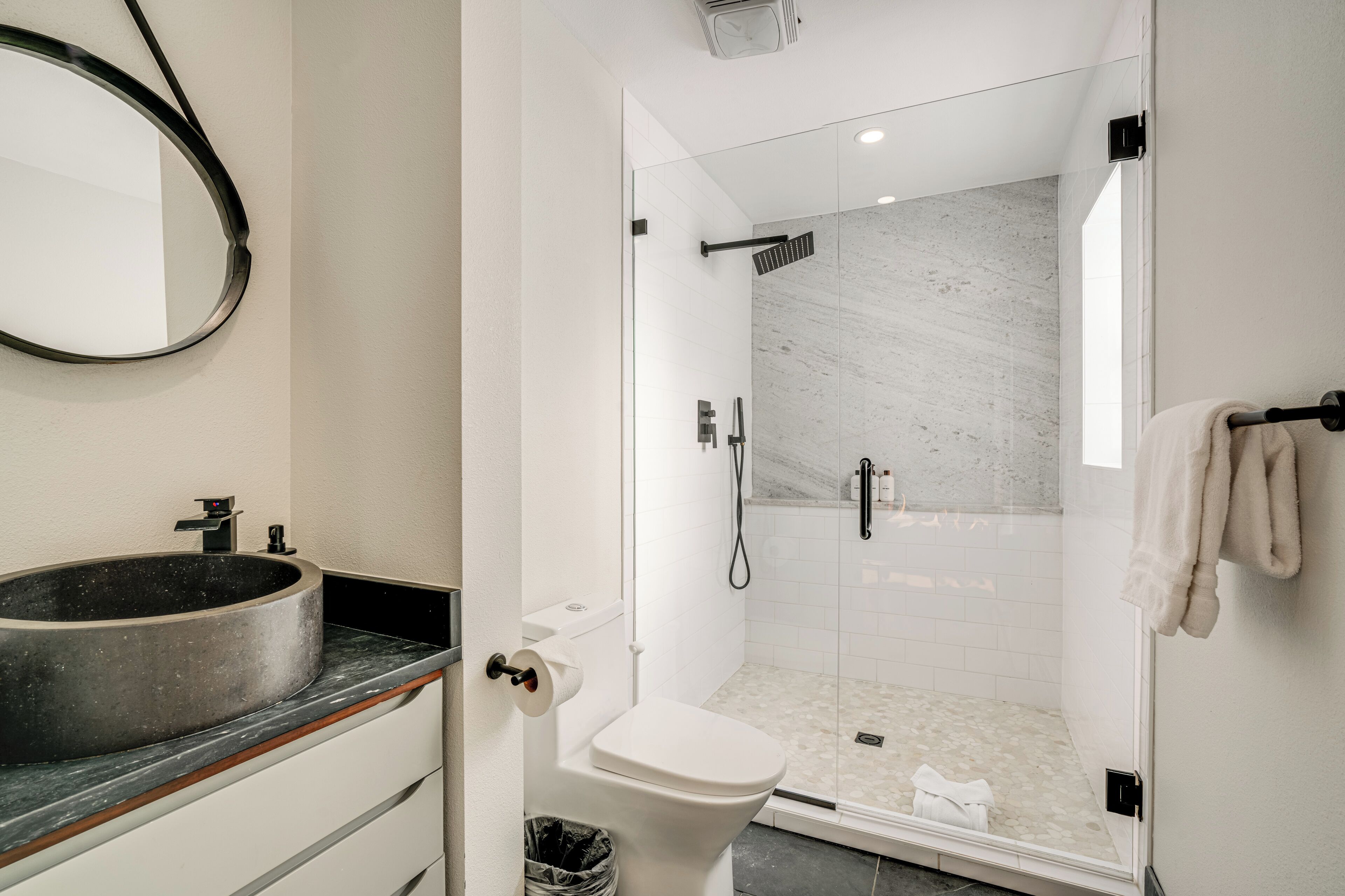 A modern bathroom with a round sink, toilet, and glass-enclosed shower.