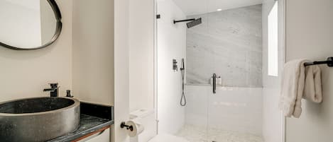 A modern bathroom with a round sink, toilet, and glass-enclosed shower.