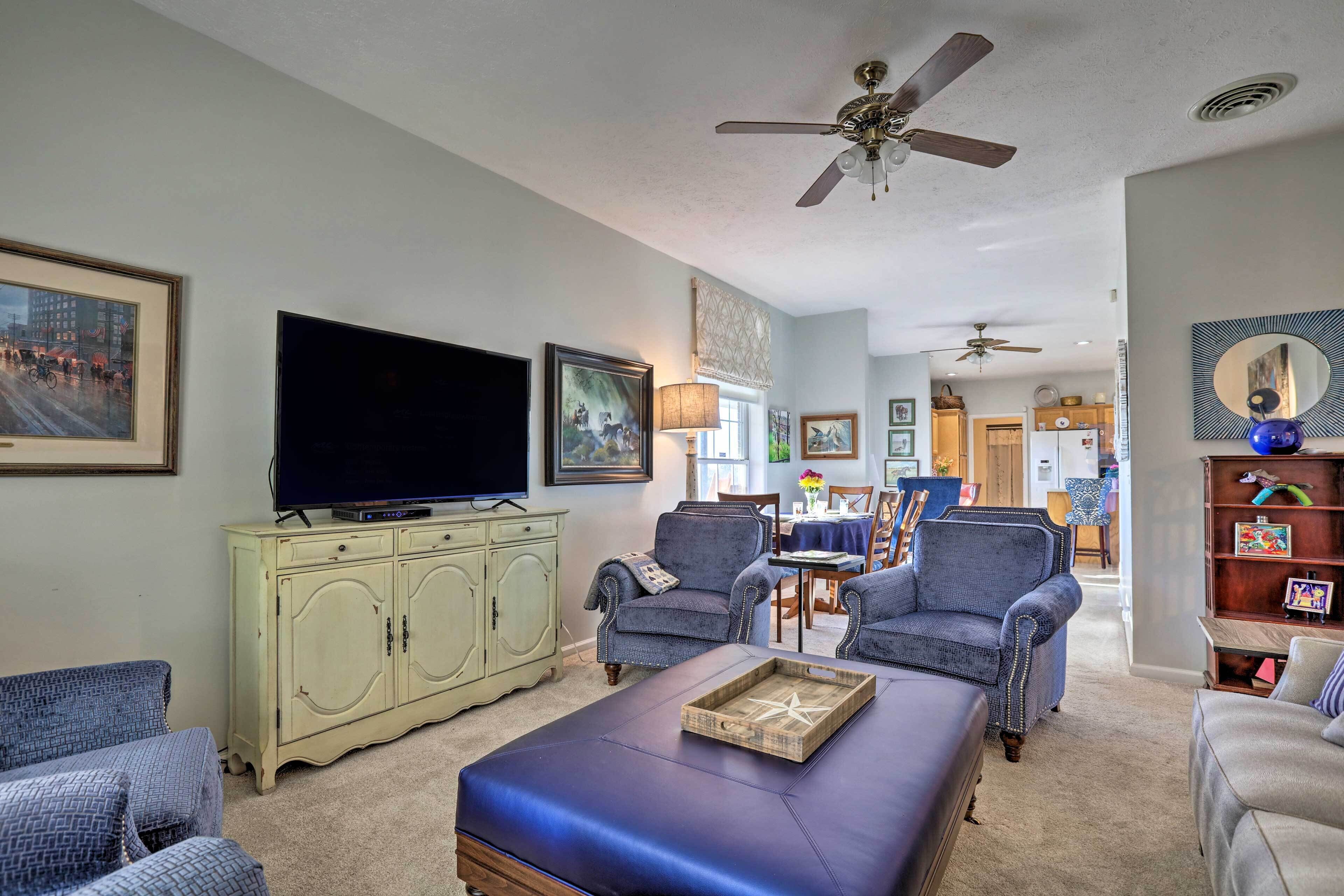A living room with a flat-screen TV, two armchairs, a sofa, a coffee table, and a ceiling fan.