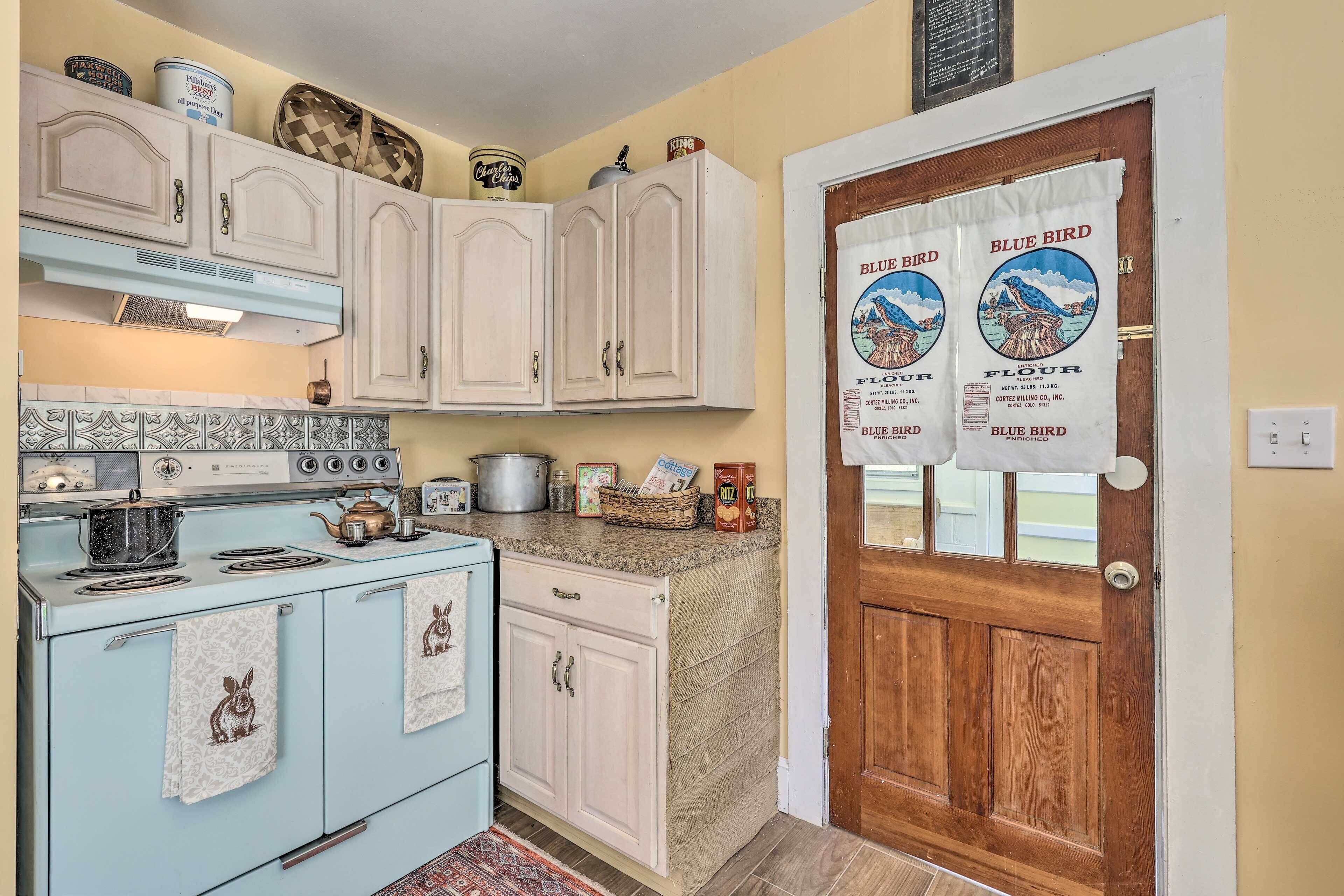 A vintage kitchen with a blue stove, white cabinets, and a wooden door with a blue bird flour sign.