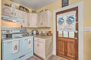A vintage kitchen with a blue stove, white cabinets, and a wooden door with a blue bird flour sign. - Fish, Bike & Hike: Blue Ridge Cottage! (Bakersville)