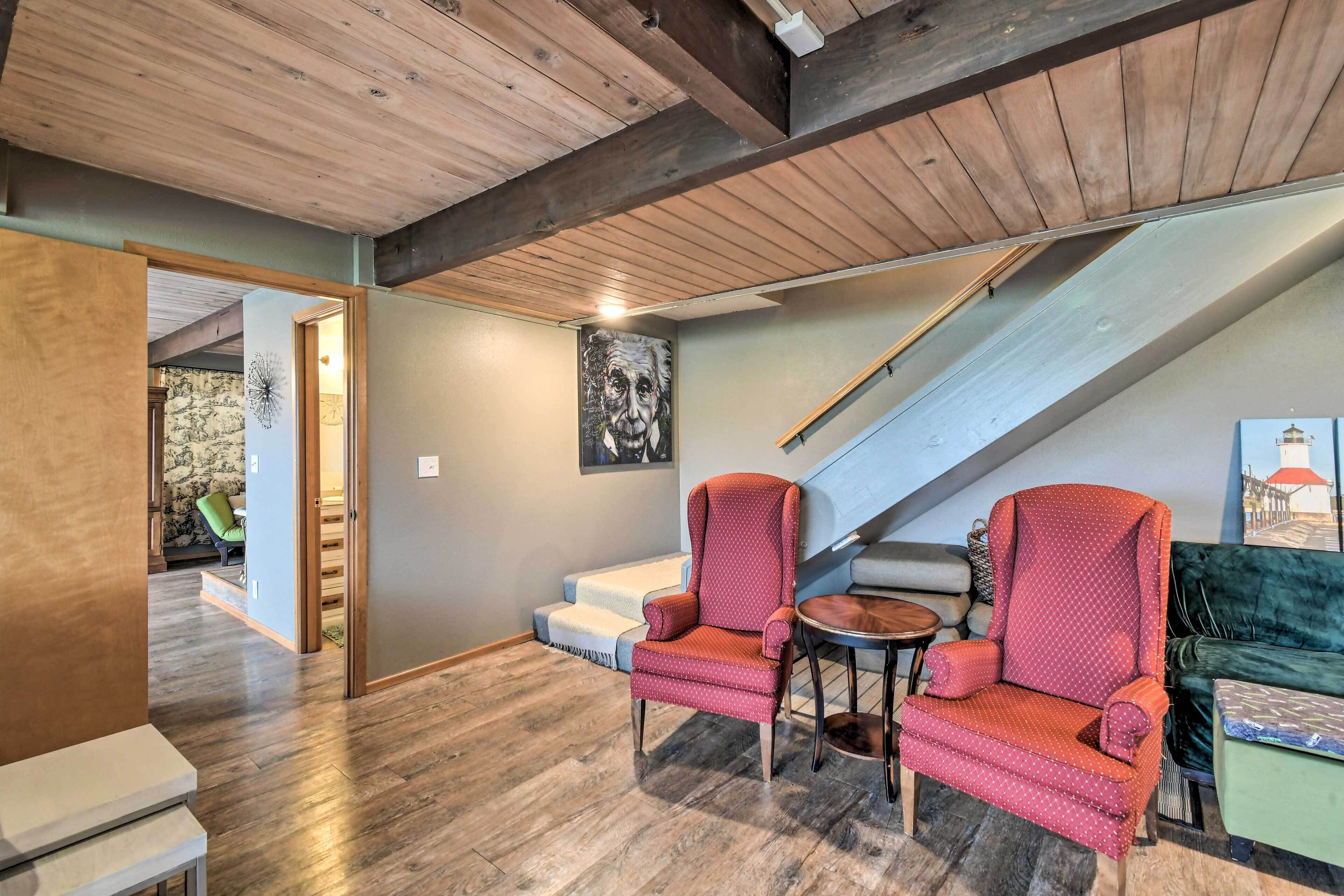 A spacious room with a wooden ceiling, a staircase, a green sofa, and two red armchairs with a small table.