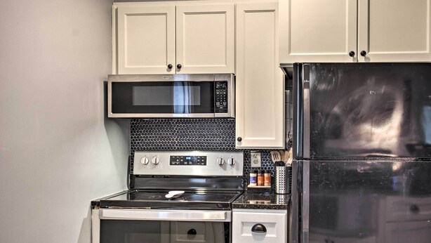 Una cucina compatta con mobili bianchi, un forno a microonde in acciaio inossidabile, un frigorifero nero e un piano cottura a gas.