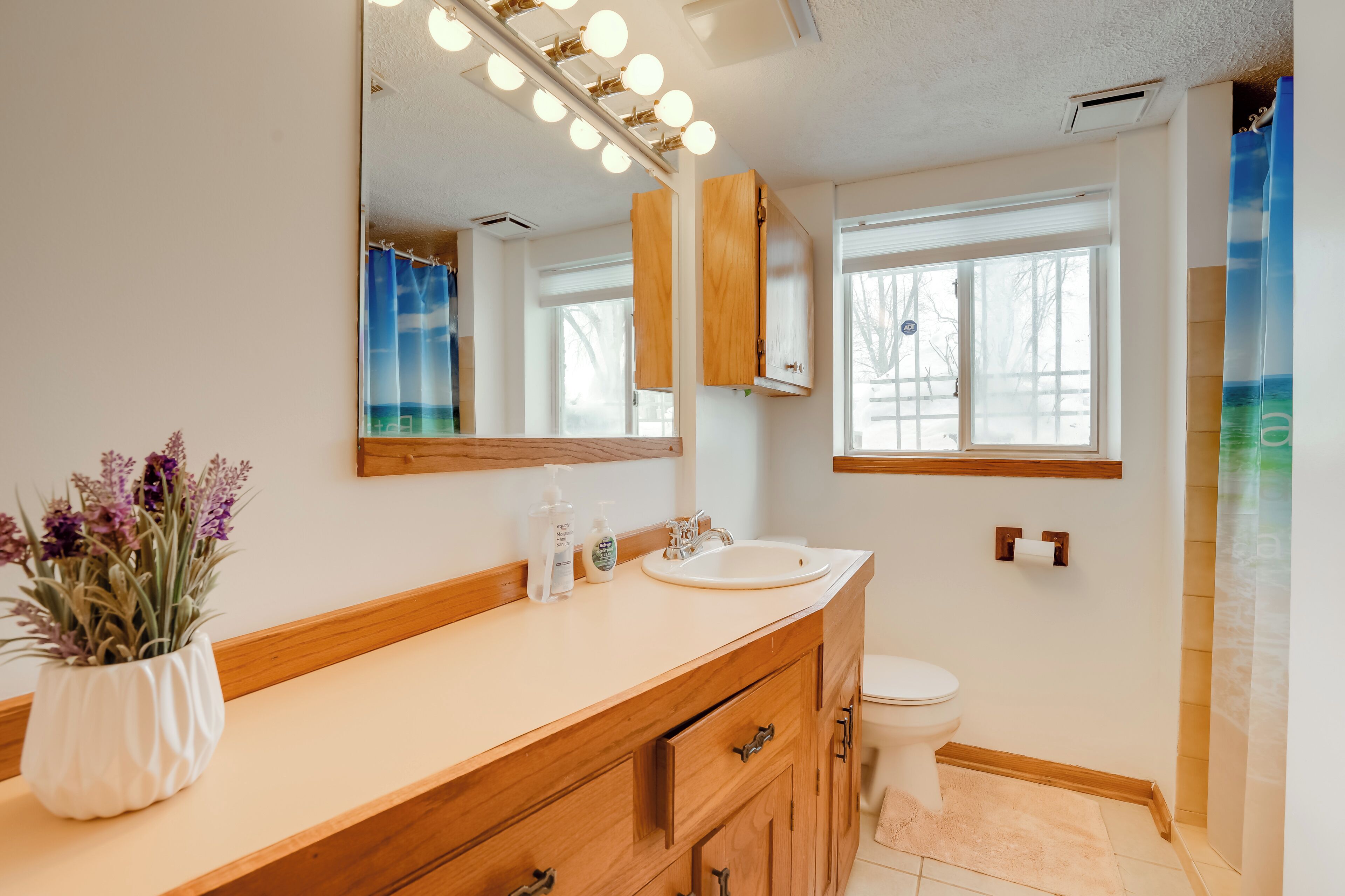 A bathroom with a wooden vanity, a large mirror, and a window.