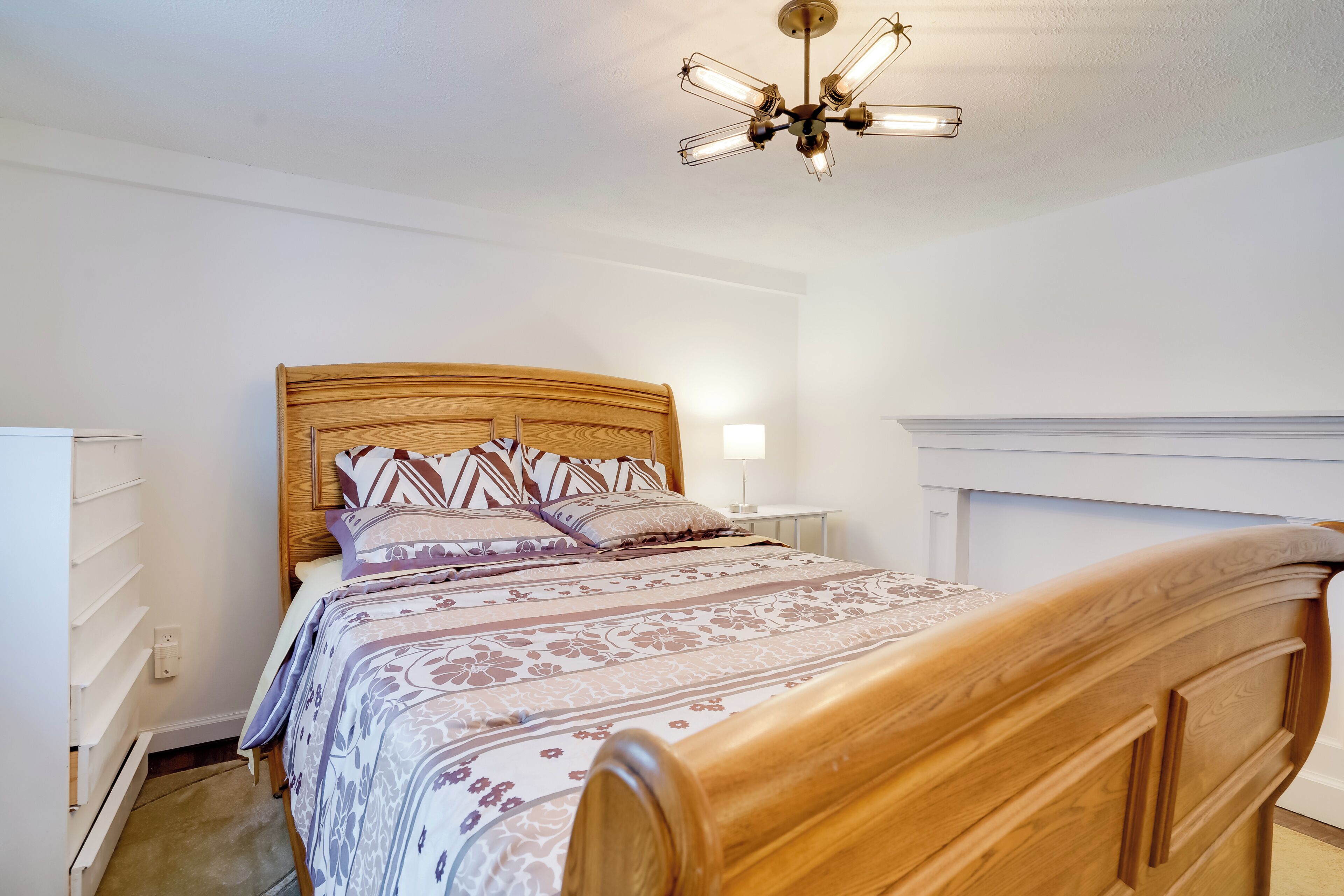 A bedroom with a wooden bed, a bedside table, a nightstand, and a ceiling fan.