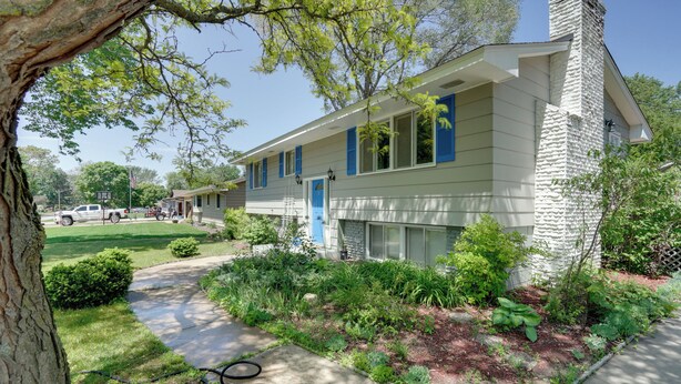 A two-story house with a stone chimney, a front porch, and a well-maintained garden. - Pet-friendly Minneapolis Apt Near Shops & Dining! (Spring Lake Park)