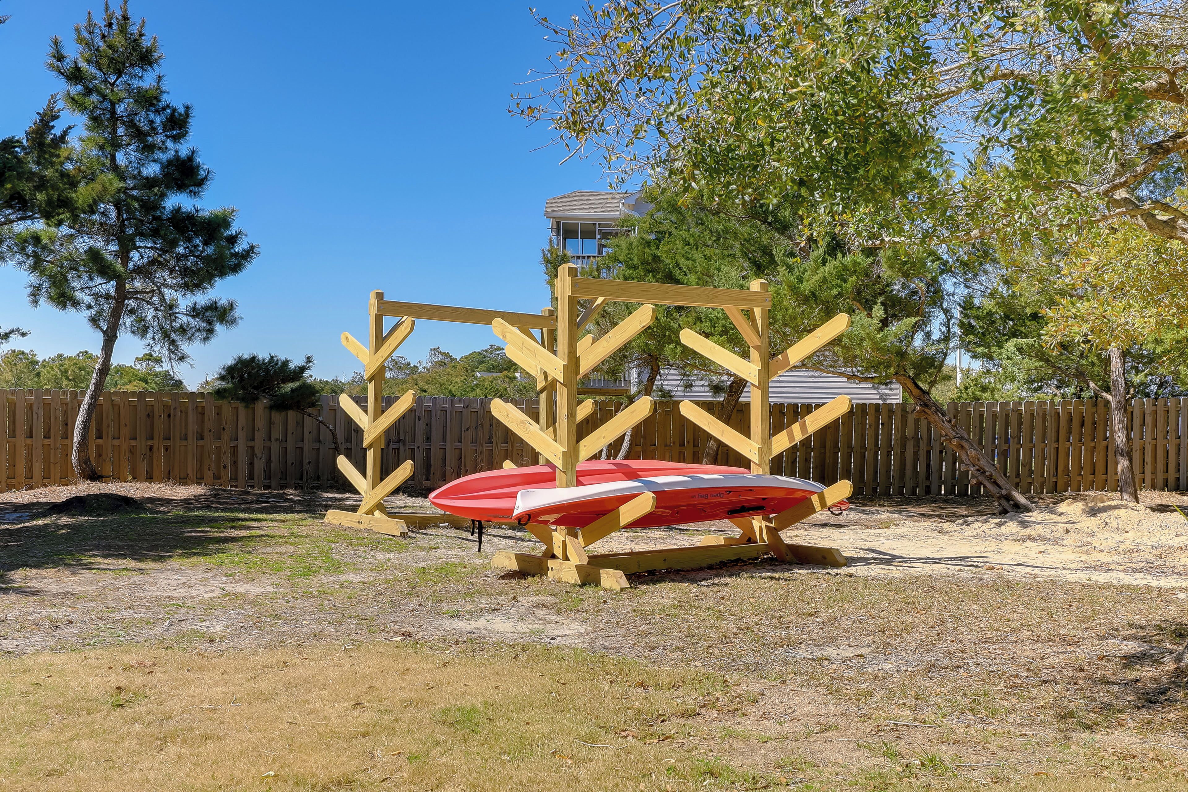 A sandy outdoor area with a wooden structure and a red and white paddleboard.