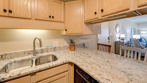 A kitchen with wooden cabinets, a granite countertop, a stainless steel sink, and a dishwasher. - Emerald Isle Vacation Rental w/ Resort Pool! (Emerald Isle)