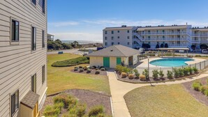 A residential building with a swimming pool, a covered patio, and a view of the ocean. - Emerald Isle Vacation Rental w/ Resort Pool! (Emerald Isle)