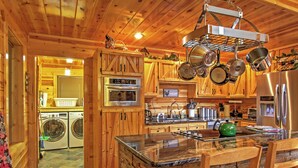A wooden cabin kitchen with a stone island, built-in oven, and hanging pots. - Hot Tub & Outdoor Kitchen: Smoky Mountain Cabin (Sevierville)
