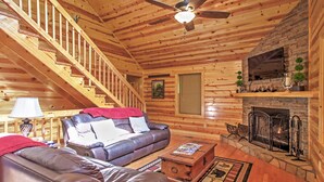 A log cabin interior with a wooden staircase, leather sofas, a fireplace, and a ceiling fan. - Hot Tub & Outdoor Kitchen: Smoky Mountain Cabin (Sevierville)