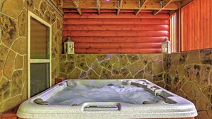 A stone-walled hot tub with a wooden ceiling and red log walls. - Hot Tub & Outdoor Kitchen: Smoky Mountain Cabin (Sevierville)