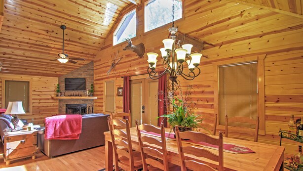 A wooden cabin interior with a dining table, chairs, a chandelier, a fireplace, and a television. - Hot Tub & Outdoor Kitchen: Smoky Mountain Cabin (Sevierville)