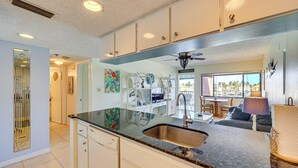 A kitchen with a granite countertop, stainless steel sink, and white cabinetry. There is a dining area with a table and chairs visible through an open doorway. - Waterfront Condo w/ Pool Access in Punta Gorda! (Punta Gorda)