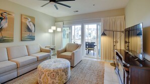 Un salon comprenant un canapé, un pouf, un ventilateur de plafond et un téléviseur posé sur un meuble en bois.